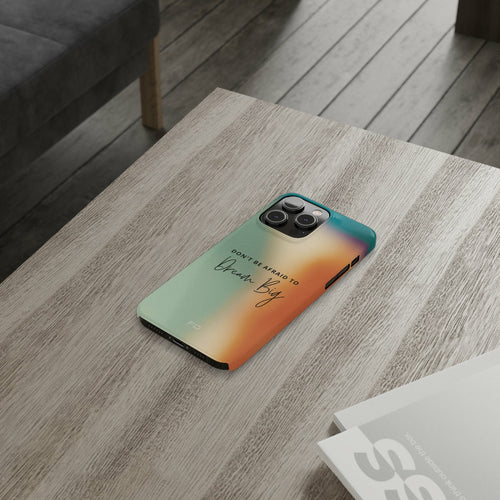 Dream Big Quote Slim Case for iPhone 14 Series resting on a wooden table with a stylish abstract design.